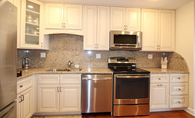 kitchen featuring decorative backsplash, light stone counters, sink, and appliances with stainless steel finishes