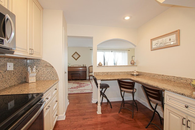 kitchen with cream cabinetry, dark hardwood / wood-style flooring, light stone countertops, and tasteful backsplash