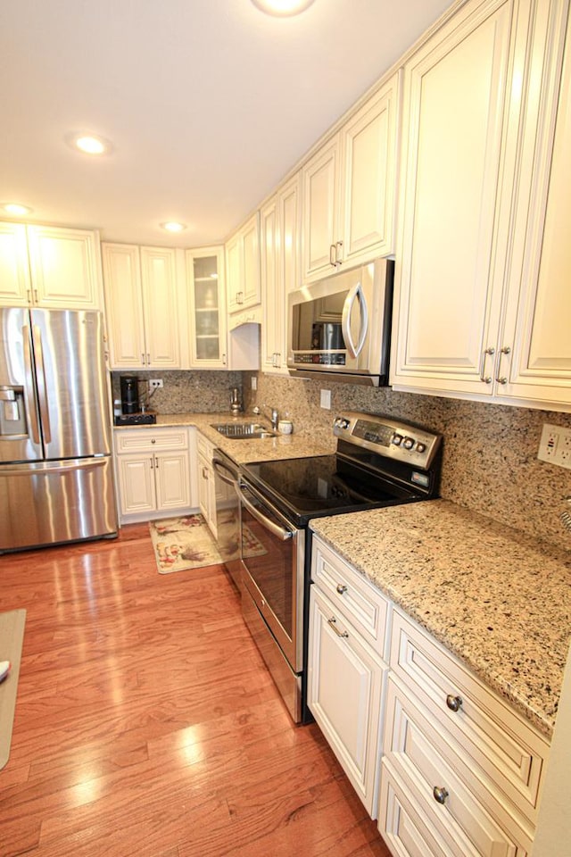 kitchen featuring sink, stainless steel appliances, light stone counters, light hardwood / wood-style flooring, and decorative backsplash