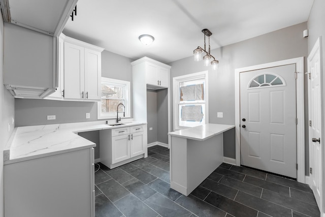 kitchen featuring pendant lighting, sink, light stone countertops, white cabinetry, and kitchen peninsula