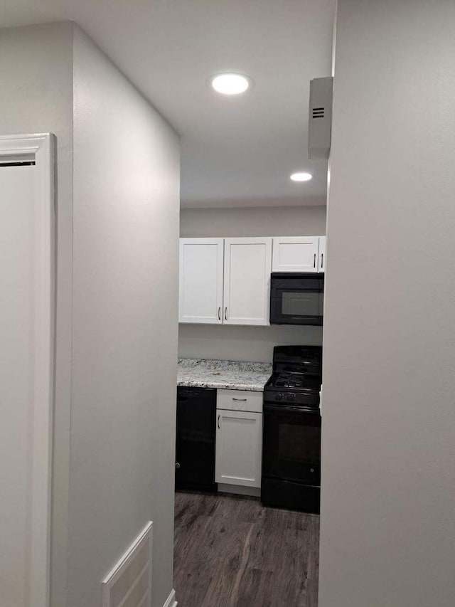 kitchen with white cabinets, dark hardwood / wood-style floors, light stone counters, and black appliances