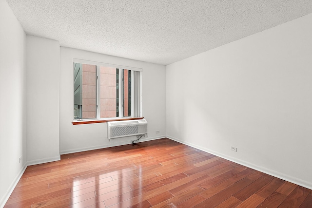 empty room featuring a wall mounted air conditioner, light hardwood / wood-style floors, and a textured ceiling