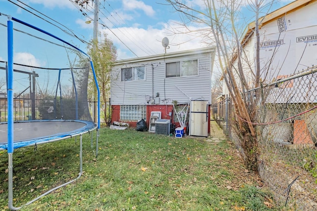 rear view of house featuring central air condition unit, a yard, and a trampoline