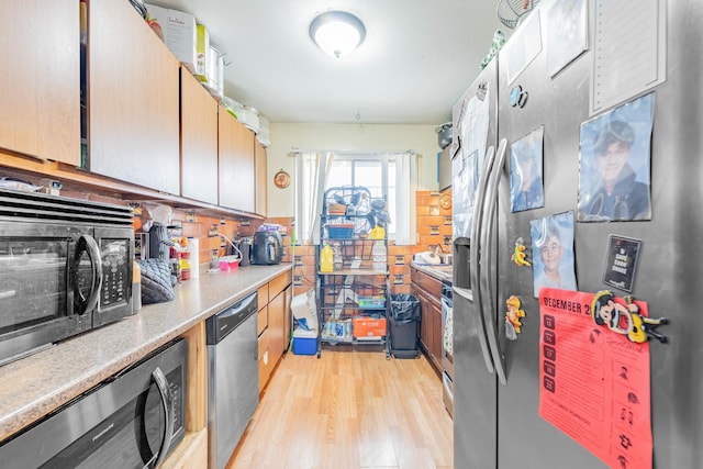 kitchen with appliances with stainless steel finishes, light wood-type flooring, and backsplash