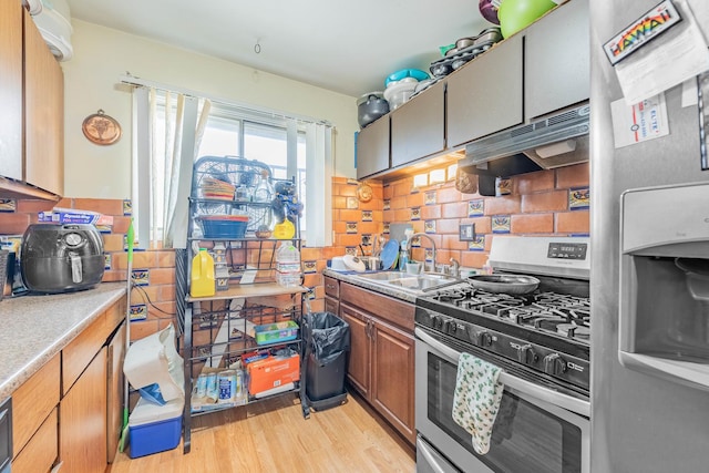 kitchen with appliances with stainless steel finishes, backsplash, light hardwood / wood-style flooring, and sink