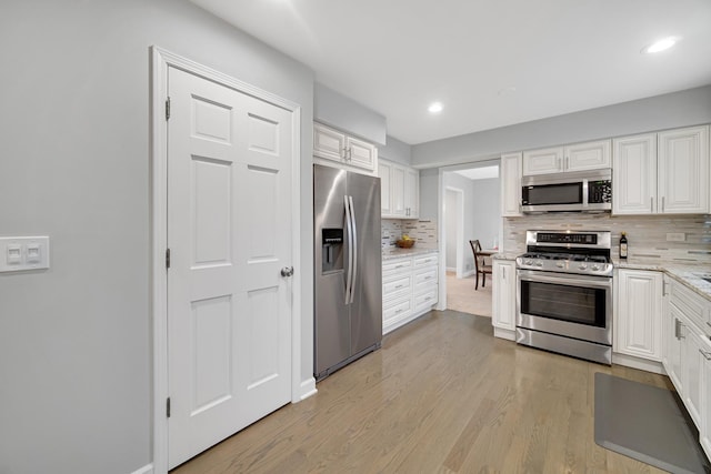 kitchen with decorative backsplash, white cabinetry, stainless steel appliances, and light hardwood / wood-style flooring