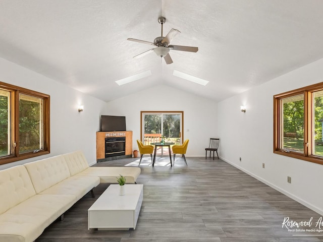 living room with a wealth of natural light, ceiling fan, lofted ceiling with skylight, and hardwood / wood-style flooring