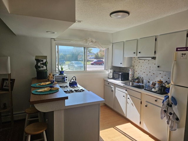 kitchen with white appliances, sink, light hardwood / wood-style flooring, white cabinetry, and a breakfast bar area