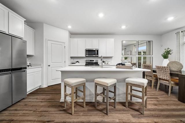 kitchen with white cabinets, dark hardwood / wood-style flooring, a kitchen island with sink, and appliances with stainless steel finishes