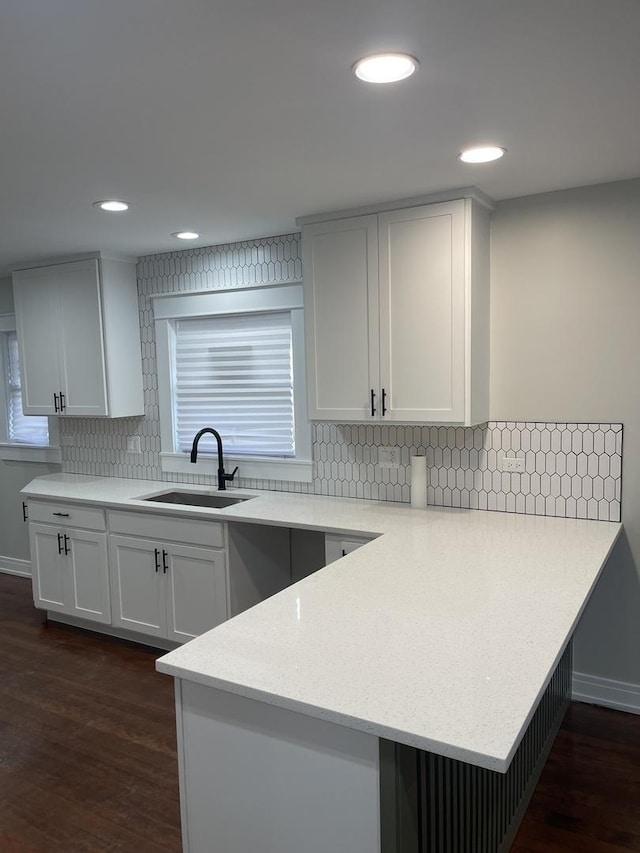 kitchen featuring kitchen peninsula, tasteful backsplash, dark wood-type flooring, sink, and white cabinetry