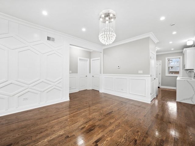 unfurnished dining area with an inviting chandelier, sink, crown molding, and dark wood-type flooring