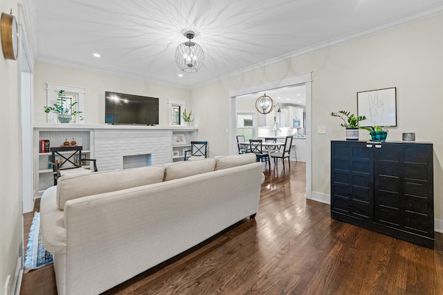 living room with a brick fireplace, dark wood-type flooring, crown molding, and a notable chandelier