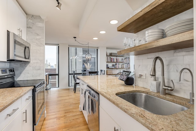 kitchen with sink, light hardwood / wood-style flooring, light stone countertops, appliances with stainless steel finishes, and white cabinetry