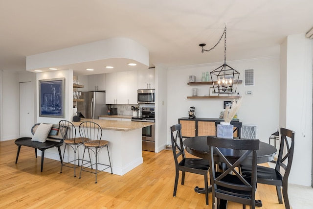 kitchen with light wood-type flooring, backsplash, ornamental molding, stainless steel appliances, and a chandelier