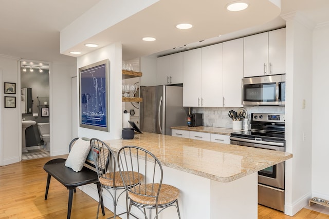 kitchen with decorative backsplash, appliances with stainless steel finishes, kitchen peninsula, white cabinets, and light hardwood / wood-style floors