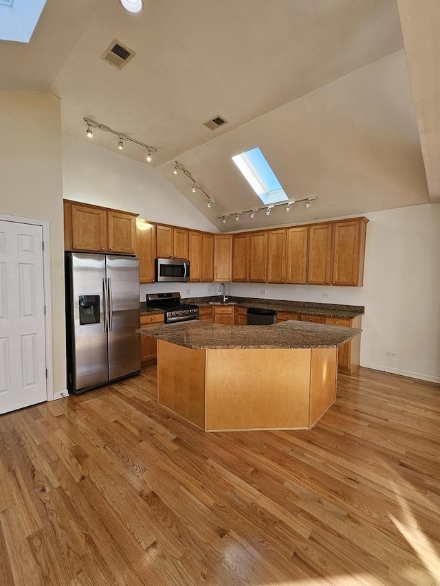 kitchen with a skylight, dark stone countertops, a center island, stainless steel appliances, and light hardwood / wood-style flooring