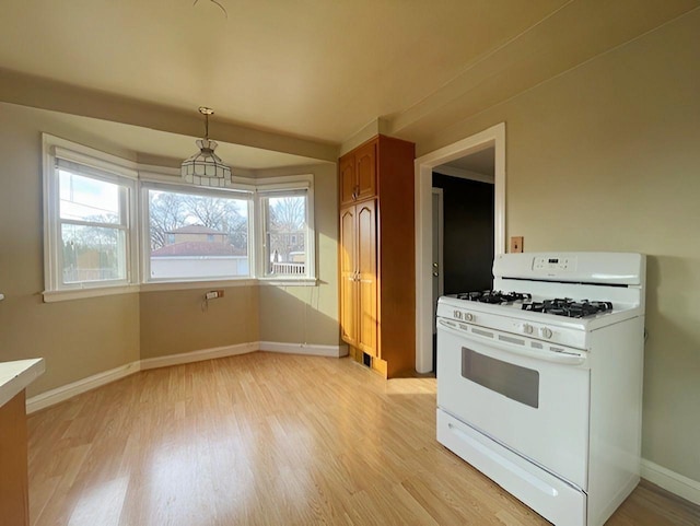 kitchen featuring decorative light fixtures, white gas range oven, and light hardwood / wood-style flooring