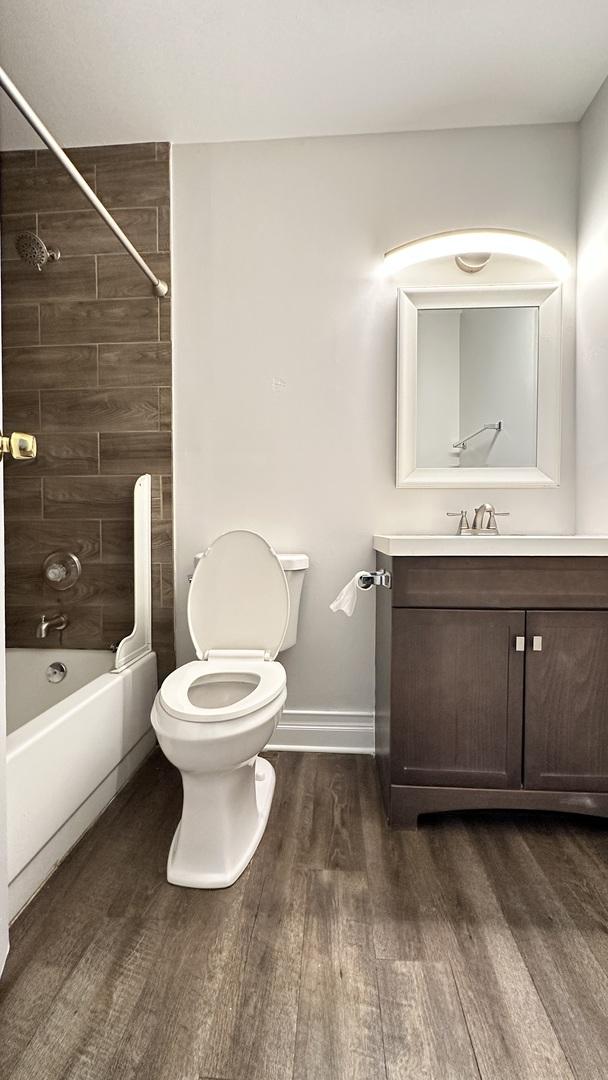 full bathroom with vanity, wood-type flooring, tiled shower / bath combo, and toilet