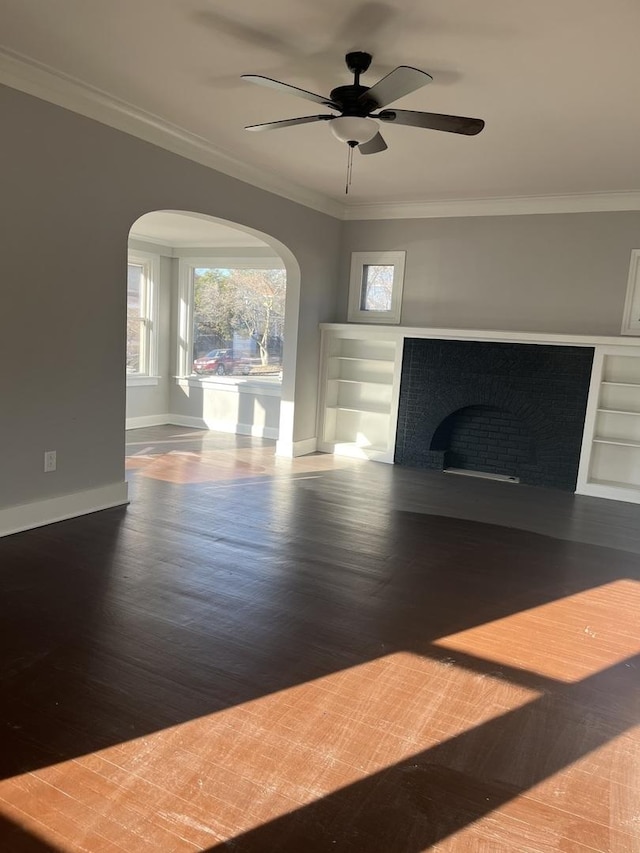 unfurnished living room with crown molding, ceiling fan, wood-type flooring, and a brick fireplace