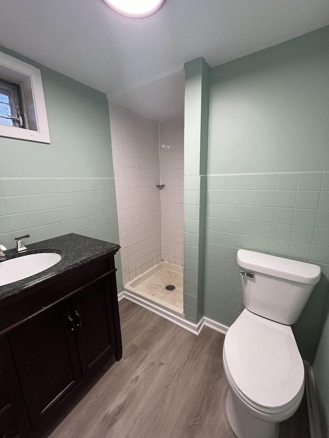 bathroom featuring a tile shower, hardwood / wood-style floors, toilet, vanity, and tile walls