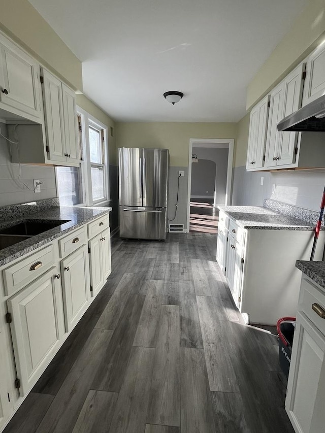 kitchen featuring white cabinets, stainless steel fridge, range hood, stone countertops, and dark hardwood / wood-style flooring