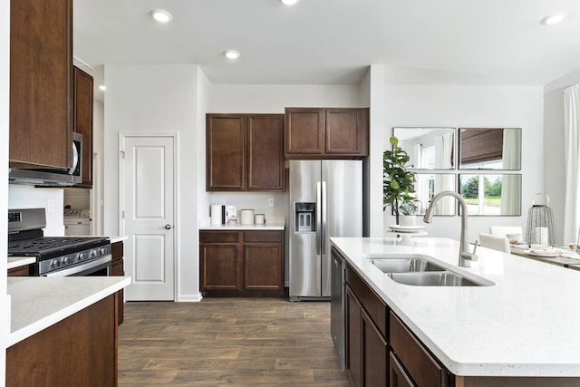 kitchen with dark wood-type flooring, sink, an island with sink, appliances with stainless steel finishes, and light stone counters