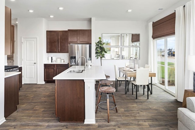 kitchen with sink, a kitchen breakfast bar, dark hardwood / wood-style flooring, stainless steel refrigerator with ice dispenser, and a center island with sink