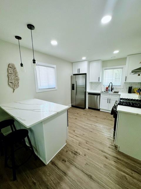 kitchen with white cabinets, appliances with stainless steel finishes, decorative light fixtures, and light hardwood / wood-style flooring