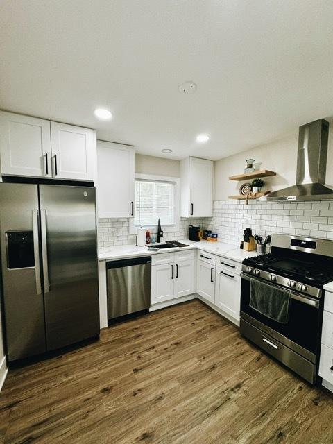 kitchen featuring white cabinets, appliances with stainless steel finishes, dark wood-type flooring, and wall chimney exhaust hood