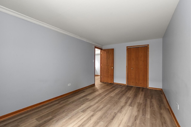 unfurnished bedroom featuring hardwood / wood-style floors, crown molding, and a closet