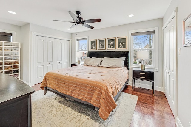 bedroom with multiple windows, ceiling fan, multiple closets, and hardwood / wood-style flooring