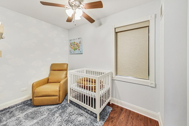 bedroom featuring a crib, dark hardwood / wood-style flooring, and ceiling fan