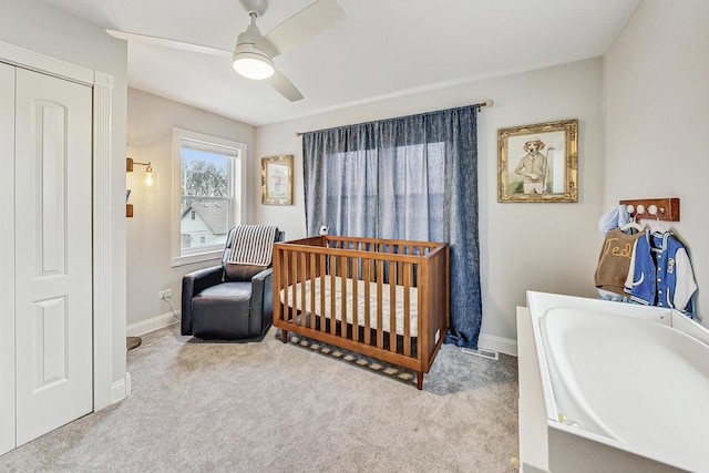 carpeted bedroom with ceiling fan, a closet, and a nursery area