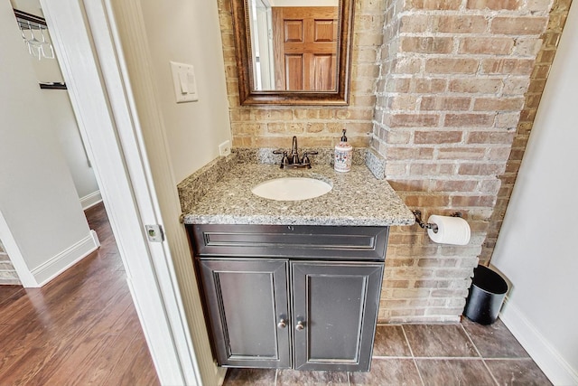 bathroom with hardwood / wood-style floors, vanity, and brick wall