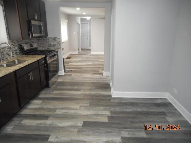 kitchen featuring backsplash, sink, hardwood / wood-style flooring, light stone counters, and stainless steel appliances