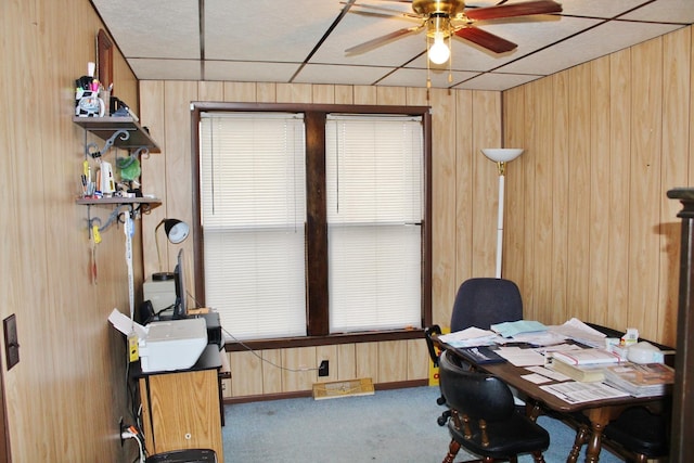 home office with ceiling fan, wooden walls, carpet floors, and a drop ceiling