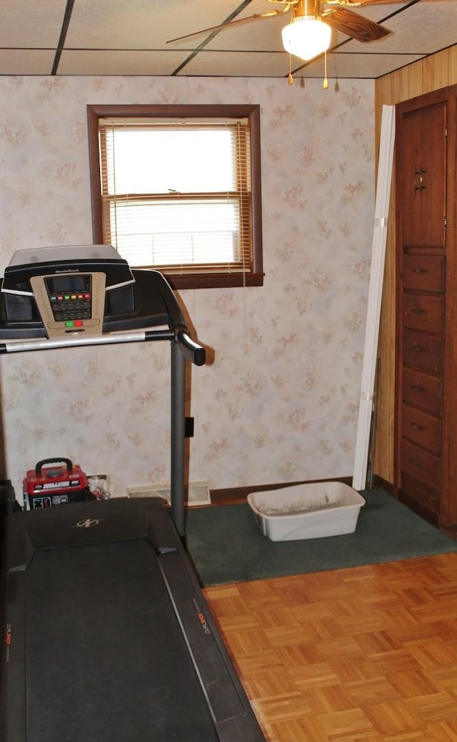 workout room with parquet floors, ceiling fan, and a wood stove