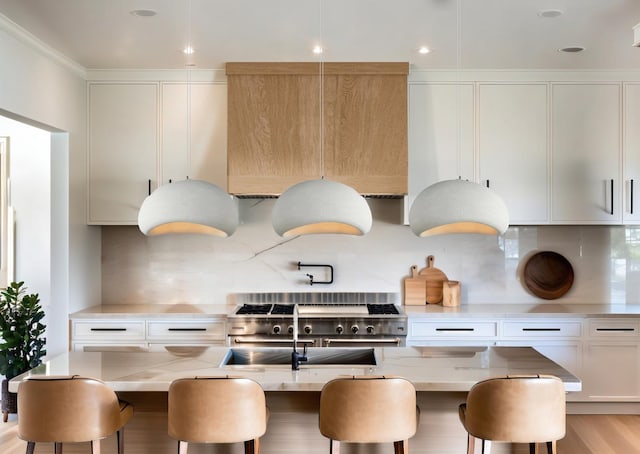 kitchen featuring a kitchen island with sink, a breakfast bar, light stone counters, white cabinetry, and backsplash