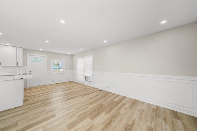 unfurnished living room with a wall mounted air conditioner and light hardwood / wood-style flooring