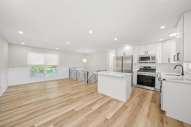 kitchen with white cabinets, sink, light hardwood / wood-style flooring, appliances with stainless steel finishes, and a kitchen island