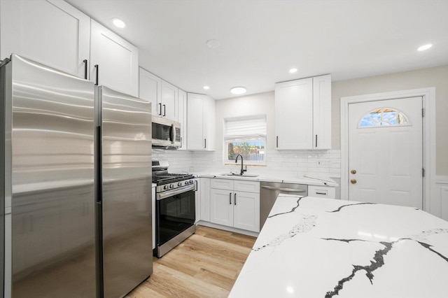 kitchen featuring white cabinets, sink, light hardwood / wood-style flooring, light stone countertops, and stainless steel appliances