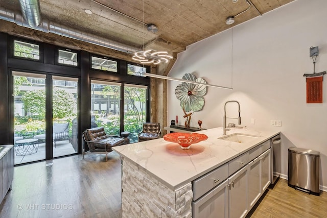 kitchen with a sink, light stone countertops, light wood-type flooring, dishwasher, and a peninsula