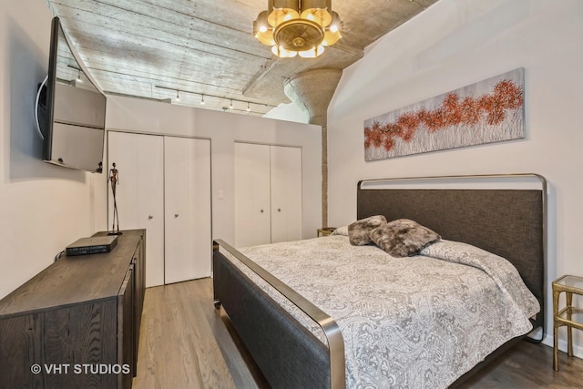 bedroom with a chandelier, light wood-type flooring, track lighting, and two closets