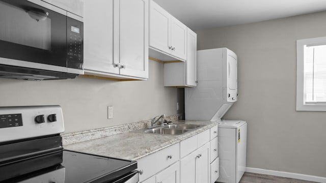 kitchen featuring hardwood / wood-style floors, stove, white cabinets, sink, and stacked washer / drying machine