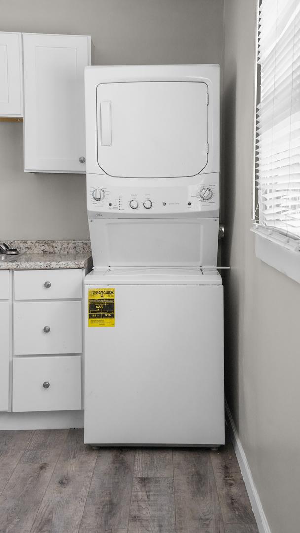 clothes washing area with cabinets, wood-type flooring, and stacked washing maching and dryer