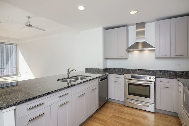 kitchen featuring wall chimney range hood, sink, light wood-type flooring, appliances with stainless steel finishes, and white cabinetry