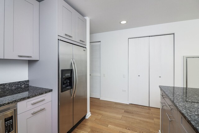 kitchen featuring built in appliances, light hardwood / wood-style floors, white cabinets, and dark stone countertops