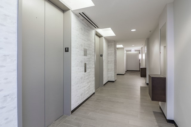 corridor featuring elevator and light hardwood / wood-style flooring