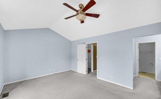 unfurnished bedroom featuring ceiling fan, lofted ceiling, a walk in closet, light carpet, and a closet