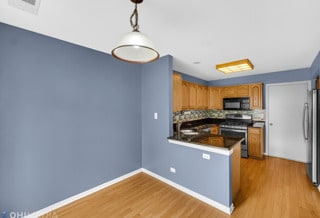 kitchen with appliances with stainless steel finishes, tasteful backsplash, decorative light fixtures, light hardwood / wood-style floors, and kitchen peninsula